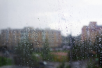 Raindrops on the window pane. Blurred outlines of houses behind.