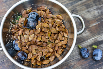 Colander with plenty off seeds of plums and two plums next to it. Cores after preparation of harvested plums for jam, baking or liqueur and Amaretto. Close-up, high angle view.
