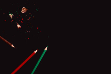 Colorful pencils with sharpening waste on dark background, side border from top view. Empty space for text.