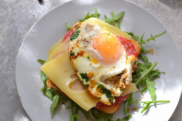 Tasty breakfast. Toast with egg, cheese and sausage. Sandwich in a white plate with arugula. View from above. Light background. Closeup