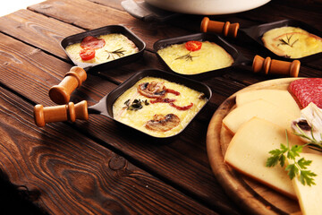 Delicious traditional Swiss melted raclette cheese served in individual skillets with salami and bacon