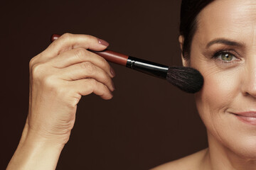 Middle aged woman applying foundation powder or blush on her face