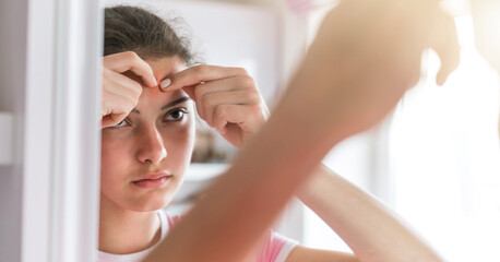 young woman with ponytail pops pimples on forehead