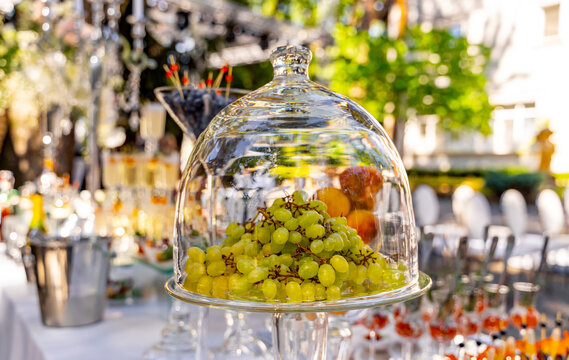 Grapes under glass transparent dome cover. Dessert on the festive table. Wedding table decoration. Selective focus.