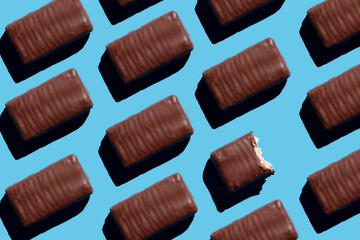 Top view of chocolate waffle candies on a blue background, one candy is bitten. Chocolate candy pattern.