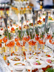 Small glasses with snacks at table. Salted appetizers on celebration. Raw with crystal glasses. Closeup.