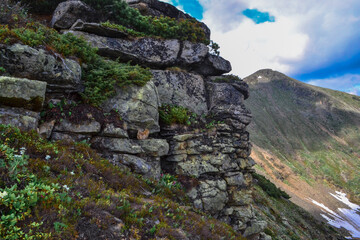 stone rock with colored moss against the background of green mountains in siberia, cloudy blue sky