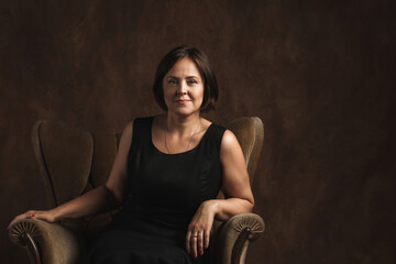 Beautiful middle aged woman sitting in a brown velvet armchair