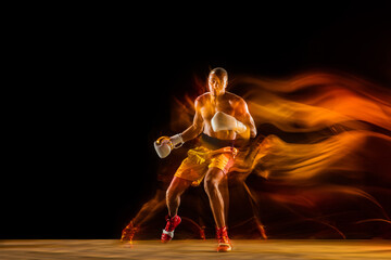 In fire. Professional boxer training isolated on black studio background in mixed light. Man in gloves practicing in kicking and punching. Healthy lifestyle, sport, workout, motion and action concept.
