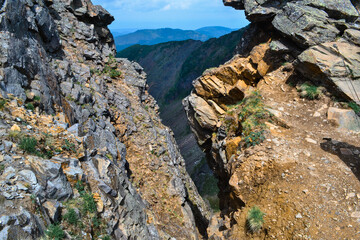stone rock gorge with colored red moss with grass on a sharp ridge in the Baikal green mountains, Siberia, Hamar-Daban, Chersky peak