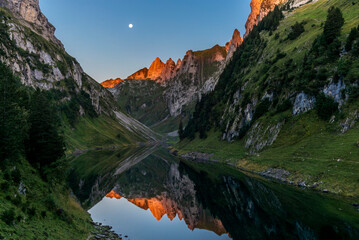 The moon and the Alpstein mountain range reflecting on the Faelensee lake in the Swiss canton of Appenzell at sunrise