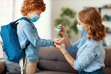 Mother disinfecting hands of schoolboy.