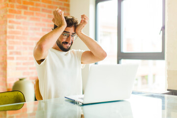 young bearded man with a laptop feeling stressed and anxious, depressed and frustrated with a...