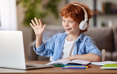 Ginger boy in headphones greeting teacher during online lesson.