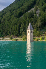 Fototapeta na wymiar The old bell tower of Curon (Graun) emerging from the emerald waters of Lake Resia, South Tyrol, Italy