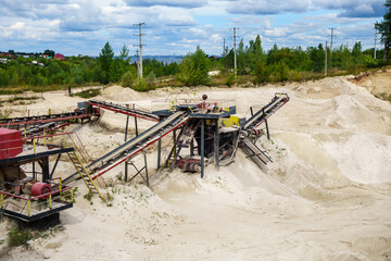 Stone crusher & conveyors in open pit mine. Dumps of processed materials in front of them