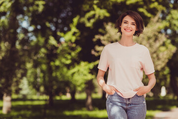 Photo of charming cute lady hands pockets toothy shiny beaming smiling walking park relaxing green trees nature healthy atmosphere chilling wear white shirt denim jeans outdoors