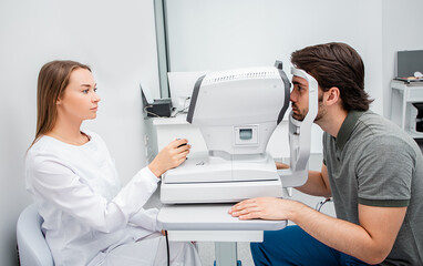 Experienced ophthalmologist using autorefractor calculate the vision correction a man patient's in a modern ophthalmic clinic.
