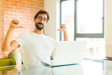 young bearded man with a laptop feeling proud, arrogant and confident, looking satisfied and...