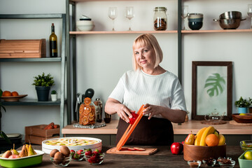 Portrait of content attractive blond-haired lady chef cooking healthy and sweet food at cozy kitchen