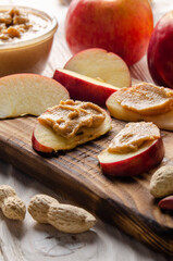 Cut board with apple slices with peanut butter on white wooden kitchen table