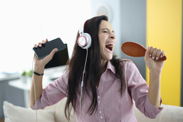 Woman with headphones and comb in her hands sings emotionally. Stress relief while singing concept
