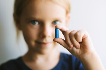 Close up portrait of a pretty little girl taking pills. Child with pills. - 376931834