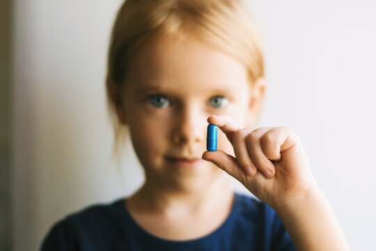 Close up portrait of a pretty little girl taking pills. Child with pills.