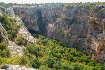 Fototapeta na wymiar Panoramic view onto bluff walls & bottom of karst sinkhole called Cennet (Heaven), Kizkalesi, Turkey. It's one of largest sinkholes in Turkey. Its depth about 70 m, square about 250x110 m