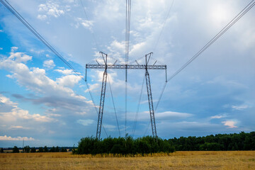 High voltage power line tower against the backdrop of a farm field and a scenic sky with clouds
