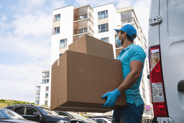 Delivery man wearing prevention mask and gloves is holding stack of the cardboard boxes