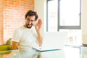 young bearded man with a laptop looking serious and curious, listening, trying to hear a secret...