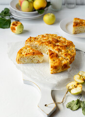 Homemade apple pie served on cutting board, yellow apples on white background