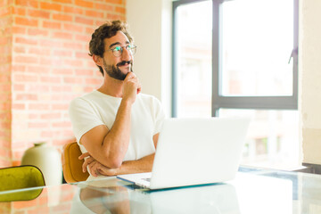 young bearded man with a laptop feeling thoughtful, wondering or imagining ideas, daydreaming and...
