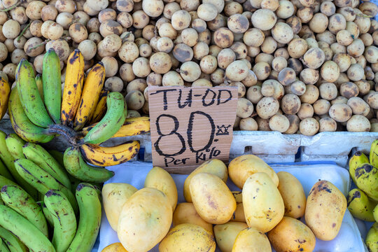 Mango, langsat and banana on farm market. Price tag with inscription Mango in cebuano language.