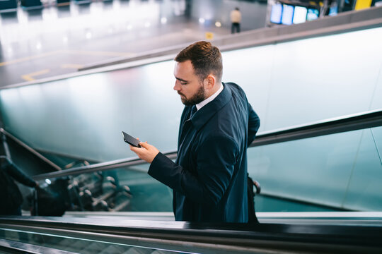 Serious man using smartphone and standing on escalator - Powered by Adobe