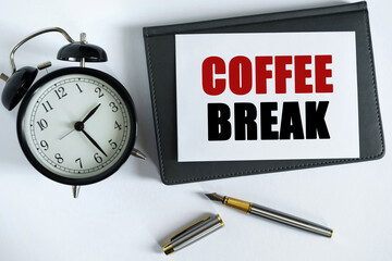 On the table there is a clock, a pen, a notebook and a card on which the text is written - COFFEE BREAK