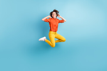 Full length photo of attractive funny lady jump high up positive emotions flight rejoicing good mood weekend wear orange shirt yellow trousers sneakers isolated blue color background