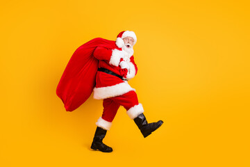 Fototapeta na wymiar Full length body size profile side view of his he nice funny cheery amazed white-haired Santa carrying big large sack custom tradition isolated bright vivid shine vibrant yellow color background