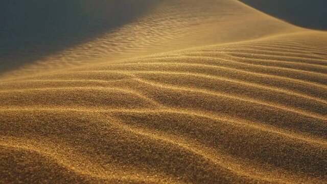 Sand waving in the wind in dunes in desert. Grains of sand move along the sand dunes. Sunset in desert. Slow motion shot