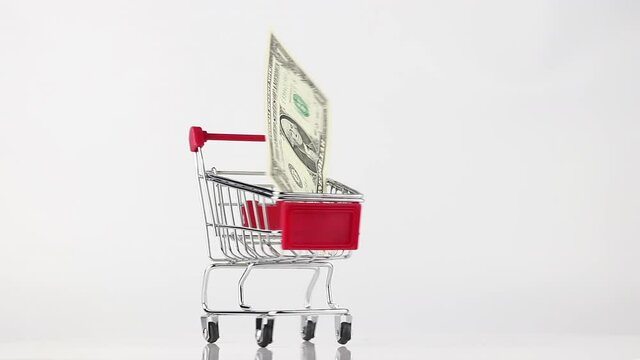 metallic shopping cart of red color with 1 dollar bill rotating against white and gray background, side view. wholesale and black friday sales concept