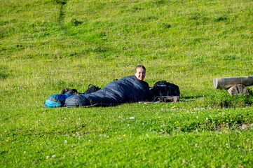 Young woman summer hiker with backpack lying in her sleeping bag on meadow after hike. Female trekker relaxing on grass in Karavanke mountains, Slovenia and Karawanken mountains, Carinthia, Austria