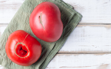 Two large red tomatoes on a light wood background, on a green napkin. Nonstandard ugly food. Copy space.