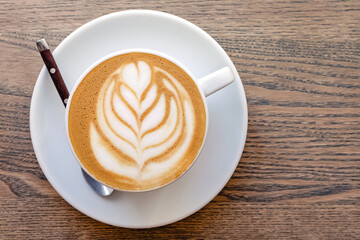 Cappuccino coffee dressing with leave shape of latte art on wood table,