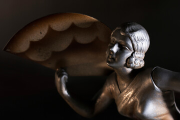 Ritratto di una giovane, elegante donna con ventaglio. Primo piano di scultura in metallo, tipico esempio di Art Decò: immagine su fondo scuro