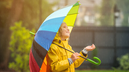 Funny little girl playing in the garden under the autumn rain. Kid wearing yellow waterproof coat...