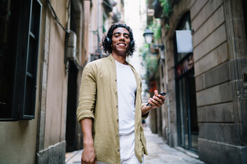 Happy African American tourist in headphones using smartphone on street