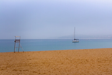 A sailboat anchored among the mist on the beach of the Bahia de Palamos, Costa Brava, Catalonia, Spain