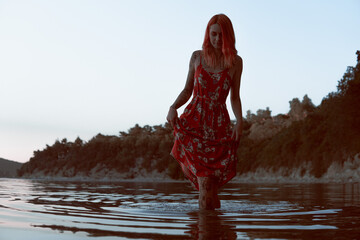 
a girl in a red dress walks in the water