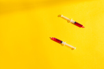 Two disposable syringes of red blood with shadows.